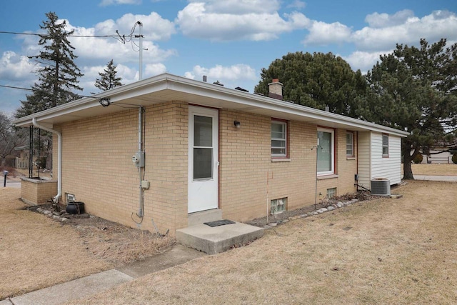 view of front of home featuring a chimney, entry steps, a front lawn, central air condition unit, and brick siding