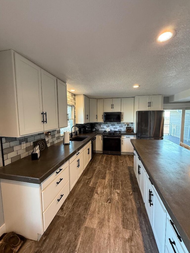 kitchen with dark countertops, dark wood finished floors, a wealth of natural light, black appliances, and a sink