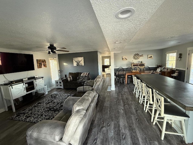 living area featuring a ceiling fan, wood finished floors, baseboards, and a textured ceiling