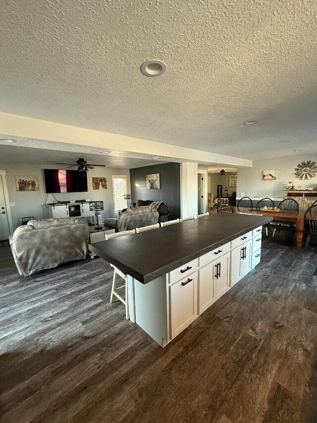 kitchen with a kitchen island, dark countertops, open floor plan, white cabinets, and dark wood-style flooring