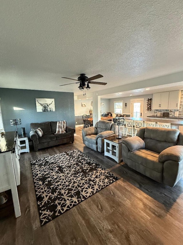 living room featuring a textured ceiling, ceiling fan, and dark wood-style flooring