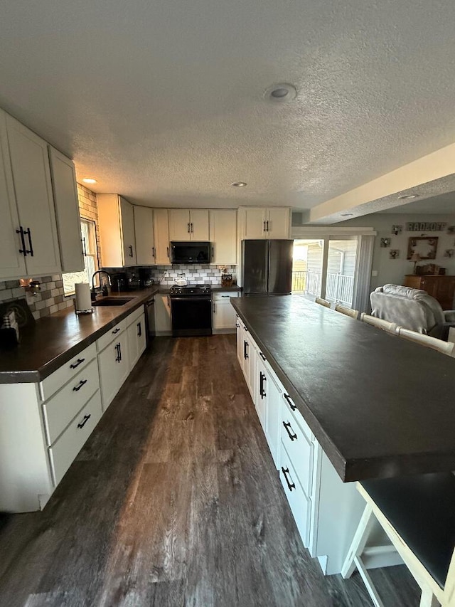 kitchen featuring black appliances, a sink, dark countertops, dark wood-style floors, and white cabinetry