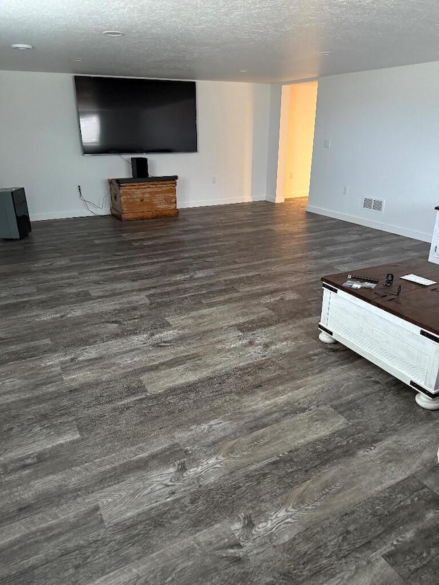 unfurnished living room featuring visible vents, baseboards, a textured ceiling, and wood finished floors