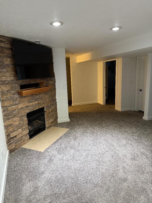 unfurnished living room with a stone fireplace, carpet, baseboards, and a textured ceiling