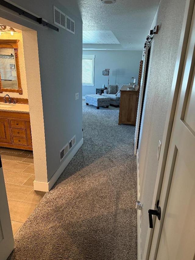 hallway with a sink, a barn door, light carpet, and visible vents