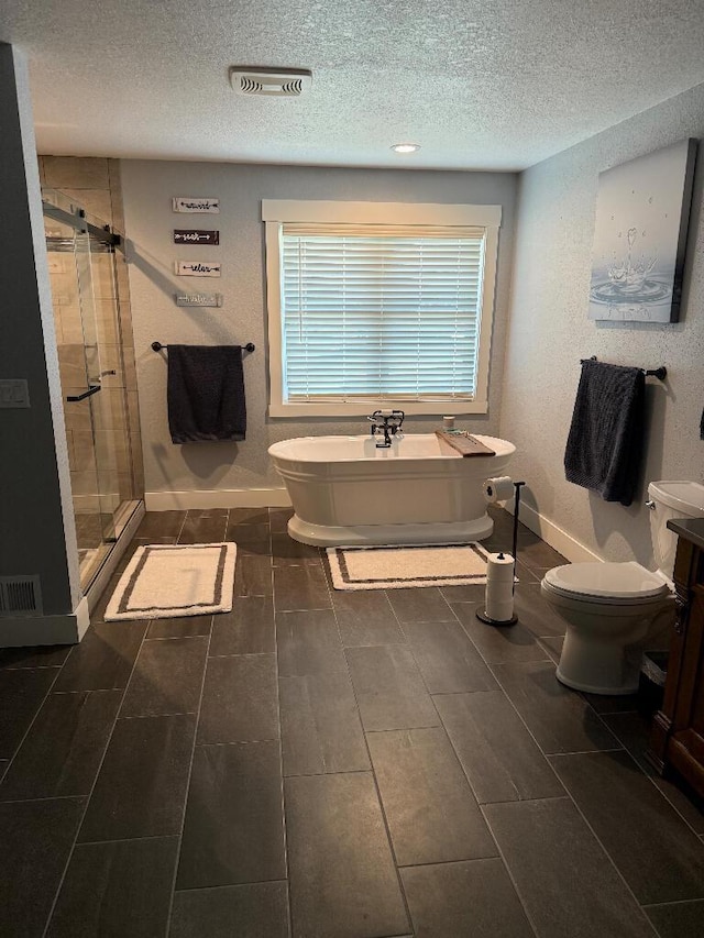 bathroom featuring visible vents, a shower stall, a freestanding bath, toilet, and a textured ceiling