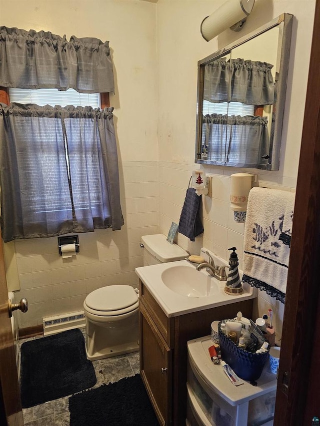 bathroom with a baseboard heating unit, a wainscoted wall, toilet, vanity, and tile walls