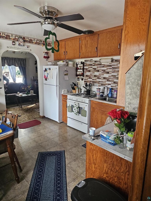 kitchen with brown cabinets, a sink, tasteful backsplash, white appliances, and dark floors