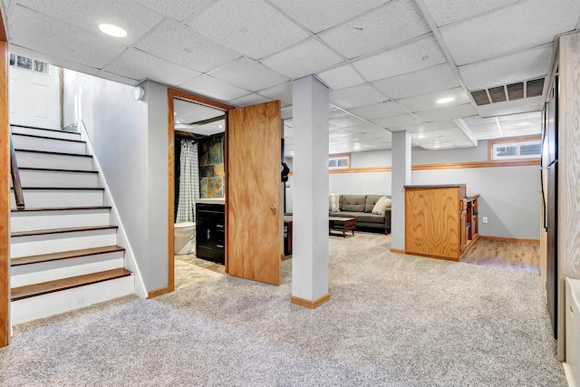 basement with carpet flooring, a paneled ceiling, stairs, and baseboards