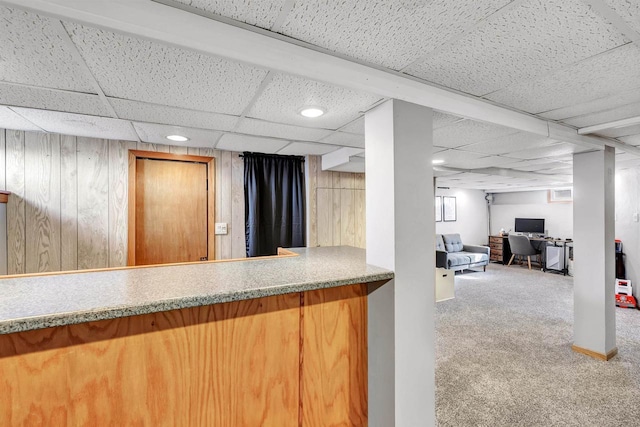 kitchen with a paneled ceiling, wood walls, and carpet flooring