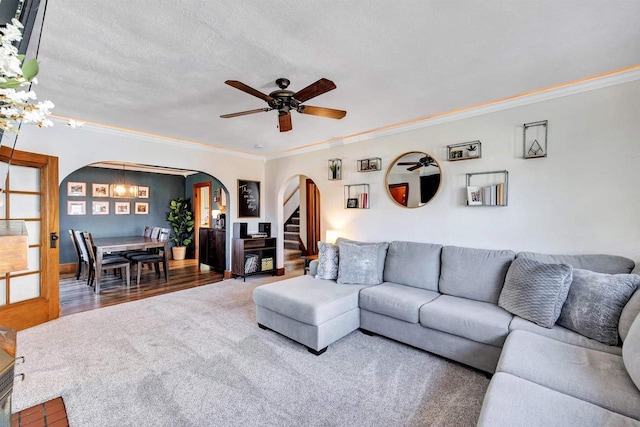 living area featuring arched walkways, ornamental molding, and ceiling fan with notable chandelier