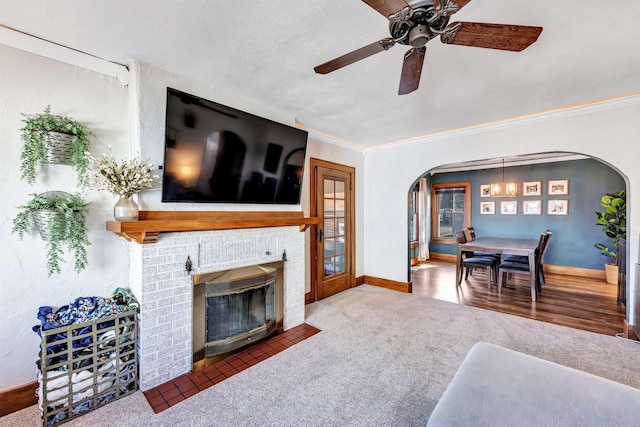 carpeted living area featuring baseboards, arched walkways, ornamental molding, and a fireplace