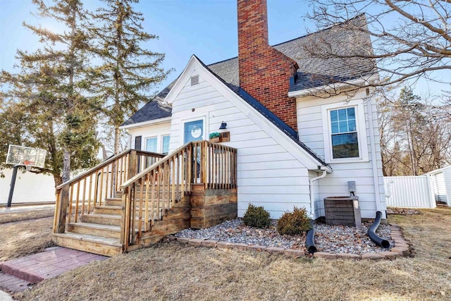 rear view of property with central air condition unit, a chimney, and roof with shingles