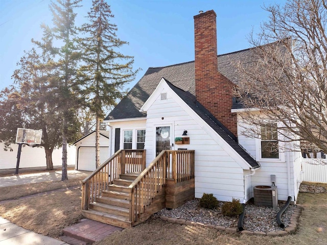 rear view of property featuring an outbuilding, cooling unit, a shingled roof, a chimney, and a garage