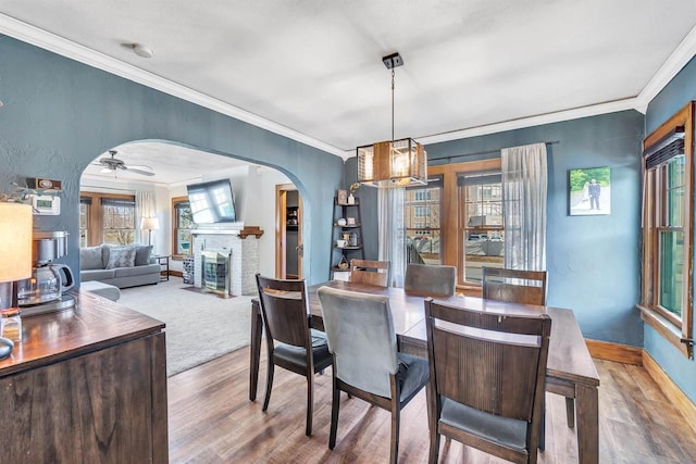 dining area with wood finished floors, arched walkways, ornamental molding, and a fireplace