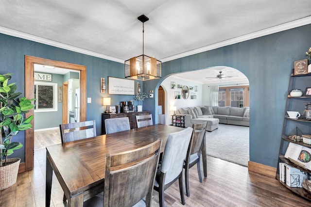 dining area with ceiling fan with notable chandelier, wood finished floors, arched walkways, crown molding, and baseboards