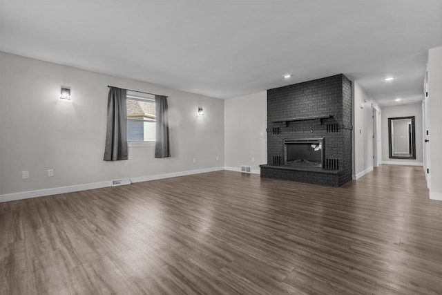 unfurnished living room with visible vents, baseboards, a brick fireplace, and dark wood-style floors