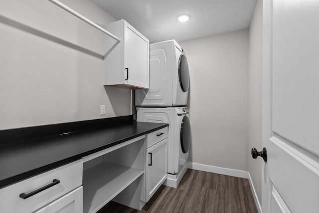 clothes washing area featuring baseboards, cabinet space, stacked washer and dryer, and dark wood-type flooring