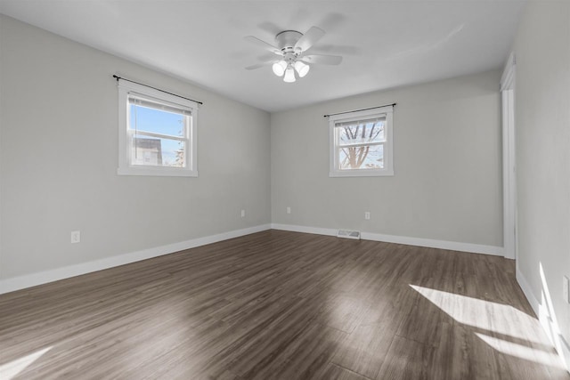 unfurnished room with visible vents, plenty of natural light, baseboards, and dark wood-style flooring