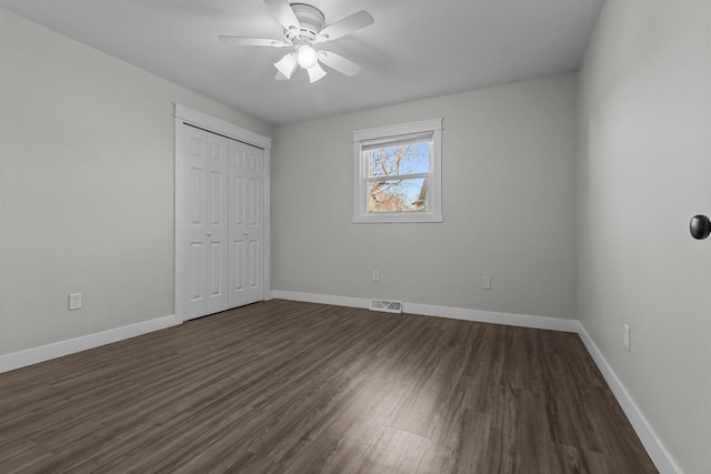 unfurnished bedroom with dark wood-style floors, visible vents, a closet, and baseboards