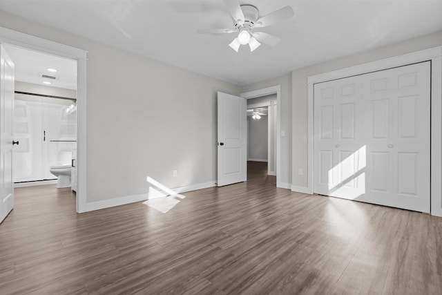 unfurnished bedroom featuring a closet, baseboards, ensuite bath, and dark wood-style flooring