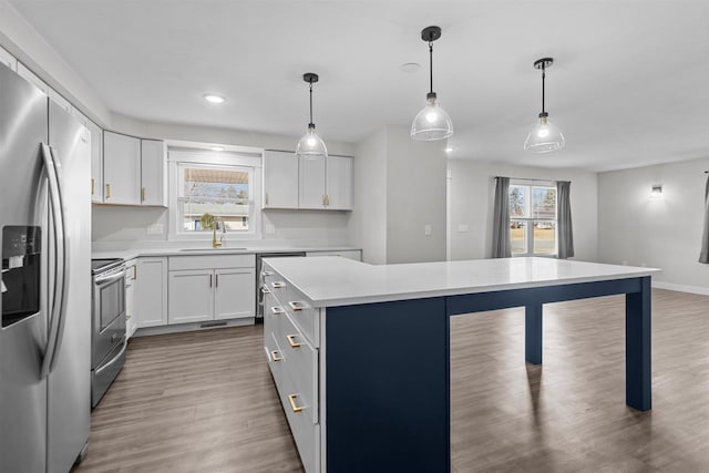 kitchen with a kitchen island, light countertops, appliances with stainless steel finishes, wood finished floors, and a sink