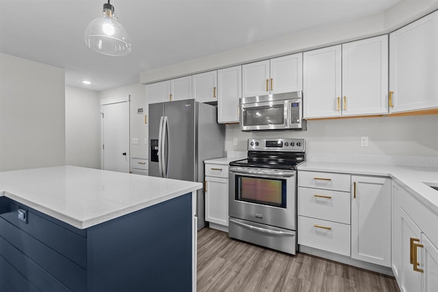 kitchen featuring light stone counters, stainless steel appliances, white cabinets, light wood finished floors, and hanging light fixtures