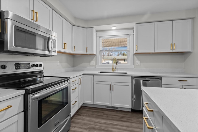 kitchen featuring a sink, appliances with stainless steel finishes, white cabinets, light stone countertops, and dark wood-style flooring