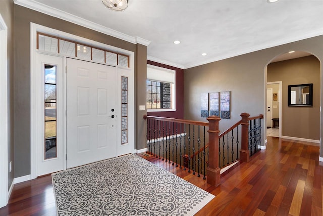 foyer entrance featuring arched walkways, ornamental molding, baseboards, and wood-type flooring