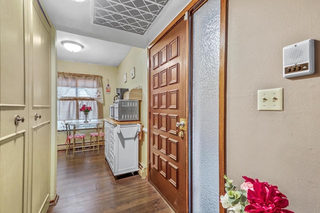 corridor with dark wood finished floors, visible vents, and a baseboard radiator