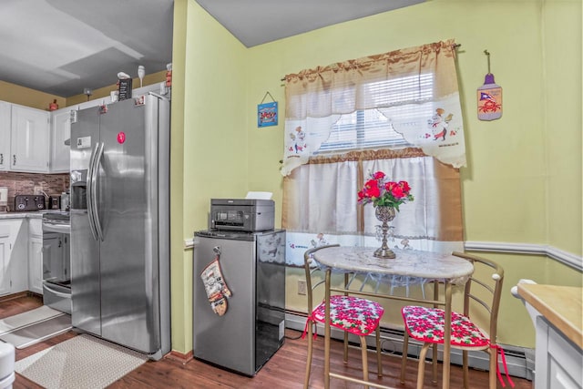 kitchen with a baseboard heating unit, backsplash, wood finished floors, white cabinetry, and stainless steel appliances