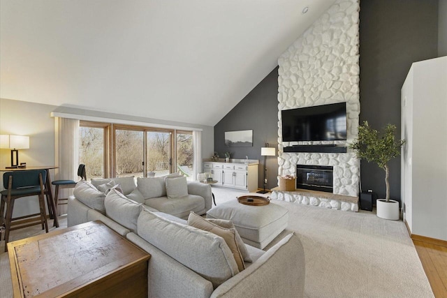 living area with baseboards, high vaulted ceiling, a stone fireplace, and light wood finished floors