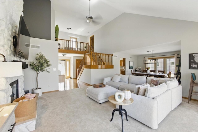 living room featuring stairway, visible vents, high vaulted ceiling, a stone fireplace, and light carpet