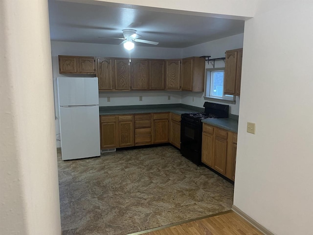 kitchen with dark wood-type flooring, a ceiling fan, dark countertops, freestanding refrigerator, and black range with gas stovetop