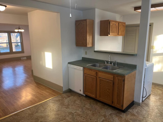 kitchen featuring dark countertops, a sink, brown cabinetry, and white dishwasher