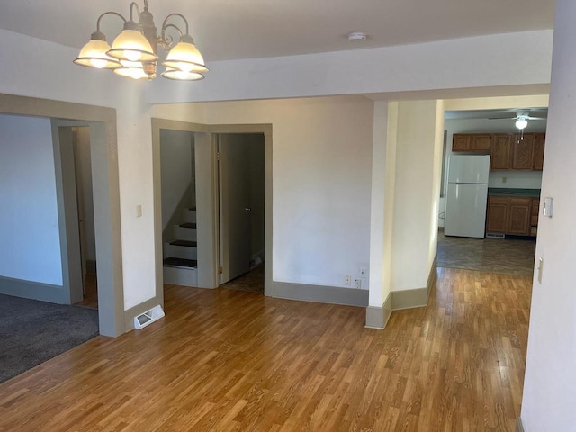 unfurnished room featuring visible vents, baseboards, stairway, light wood-style flooring, and an inviting chandelier