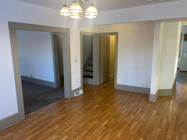 spare room with stairway, wood finished floors, visible vents, baseboards, and a notable chandelier