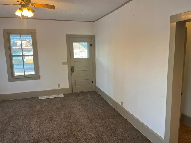 entrance foyer featuring visible vents, ornamental molding, a ceiling fan, dark colored carpet, and baseboards