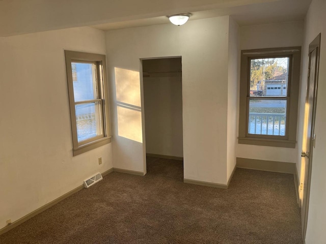 unfurnished bedroom with visible vents, a walk in closet, baseboards, a closet, and dark colored carpet