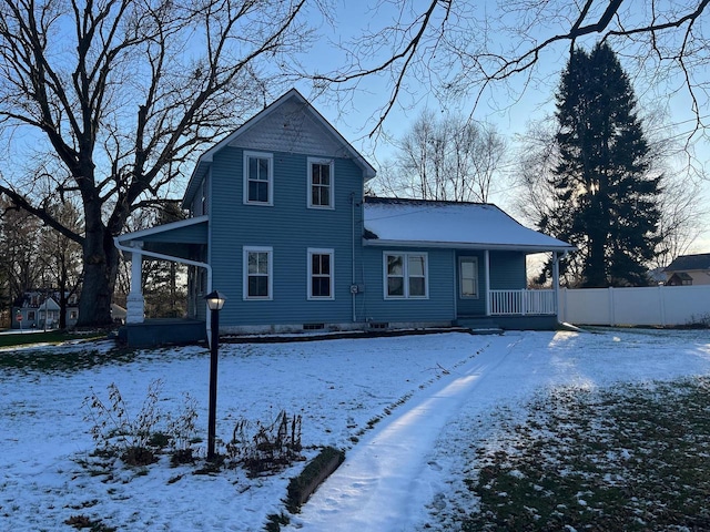 snow covered back of property with a carport, a porch, and fence