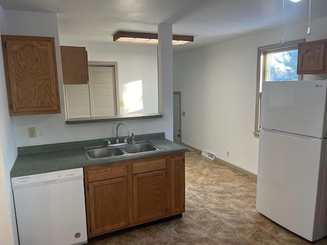 kitchen with dark countertops, visible vents, brown cabinetry, white appliances, and a sink