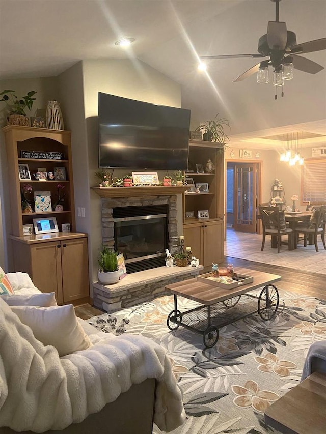 living area with a stone fireplace, light wood-style flooring, high vaulted ceiling, and ceiling fan