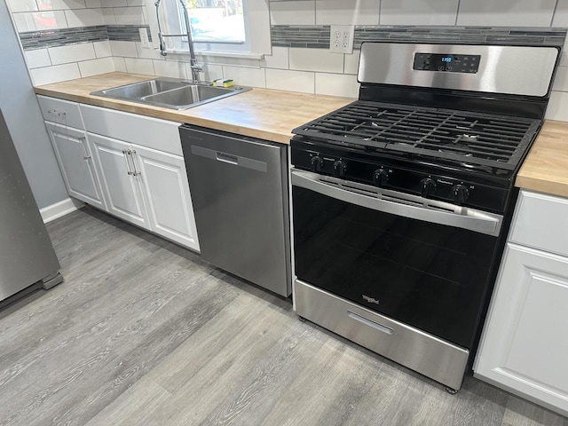 kitchen with light wood-style flooring, a sink, stainless steel appliances, backsplash, and butcher block counters