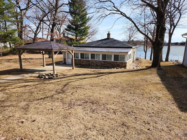 exterior space featuring a water view, a gazebo, a chimney, a carport, and stone siding