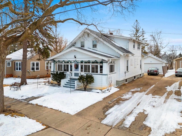 snow covered back of property featuring driveway and a detached garage