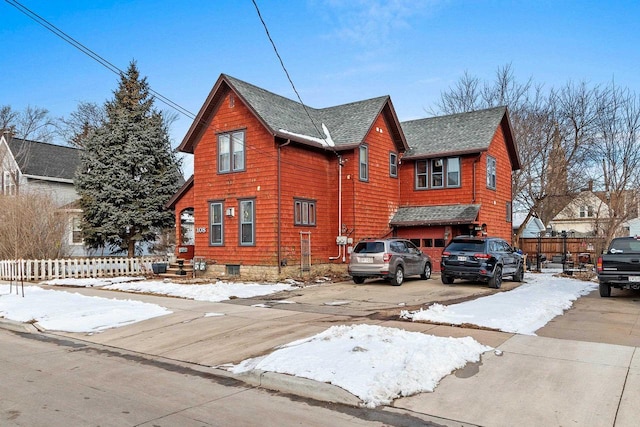 view of snowy exterior featuring roof with shingles, driveway, and fence