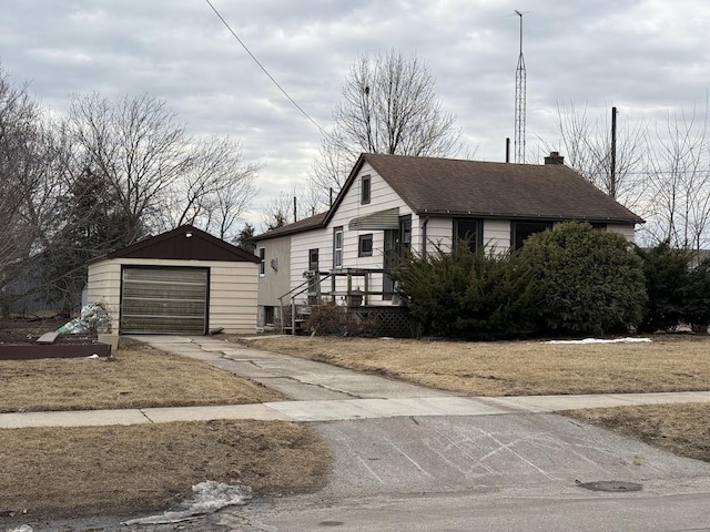 view of front facade featuring a shingled roof, a chimney, an outdoor structure, concrete driveway, and a detached garage