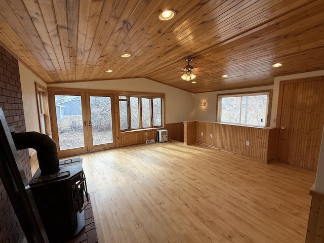 interior space featuring wood ceiling, lofted ceiling, wainscoting, a wood stove, and plenty of natural light