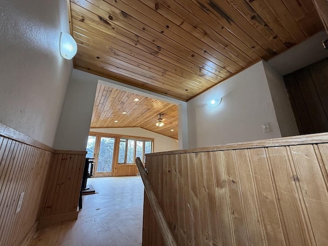 hall featuring wooden walls, wooden ceiling, concrete floors, and vaulted ceiling