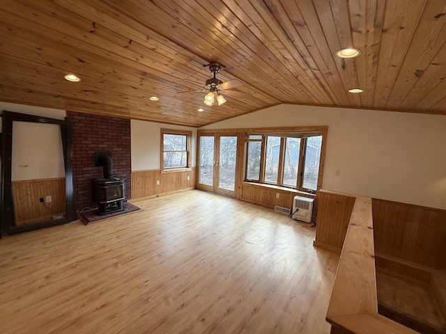 unfurnished living room with lofted ceiling, light wood-style flooring, a wood stove, wood ceiling, and wainscoting